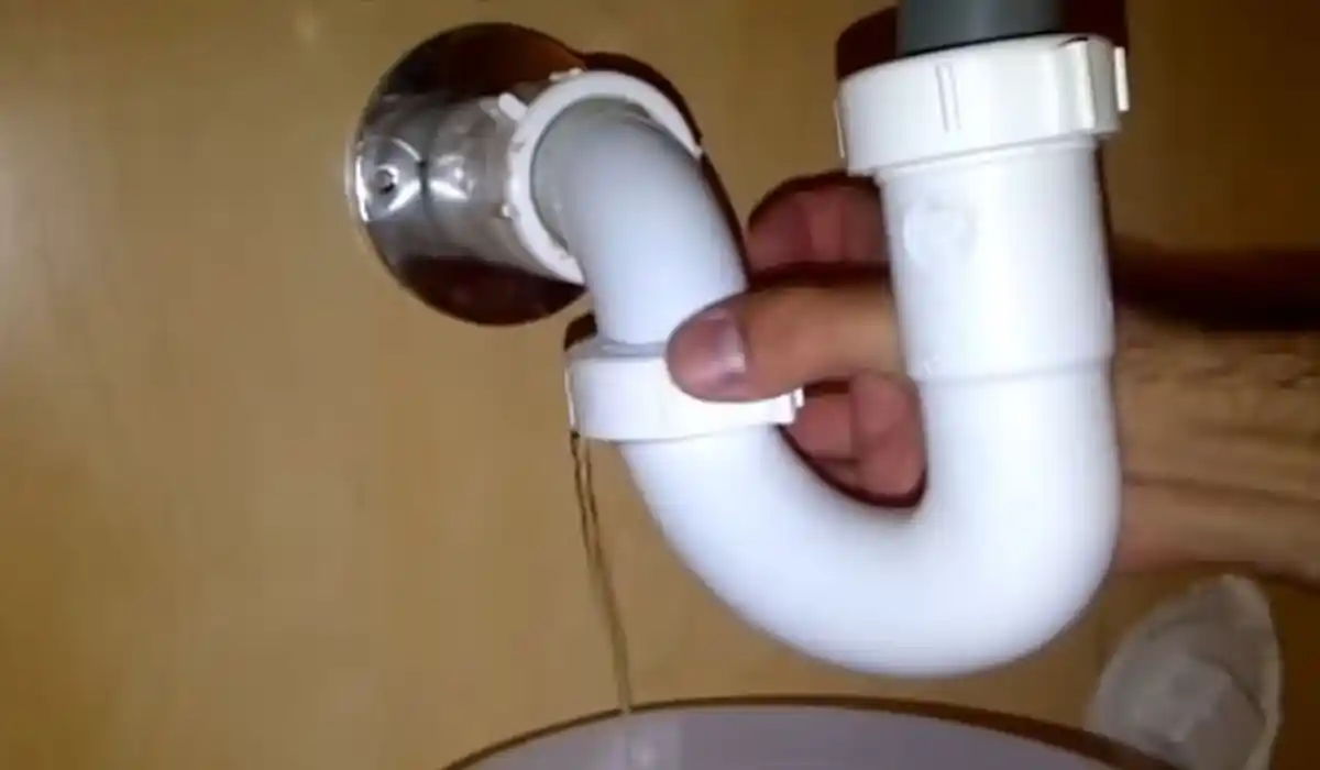 Hand repairing a leaking pipe fitting under a sink