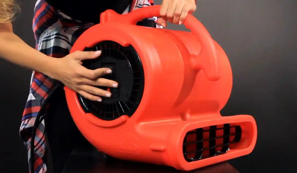 Hands positioning a red air mover fan for flood cleanup drying