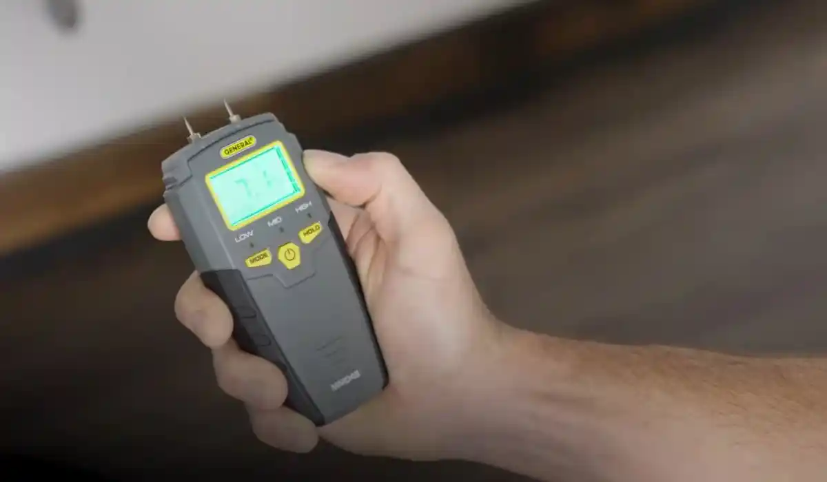 Hand holding a moisture meter device near a ceiling during a mold inspection